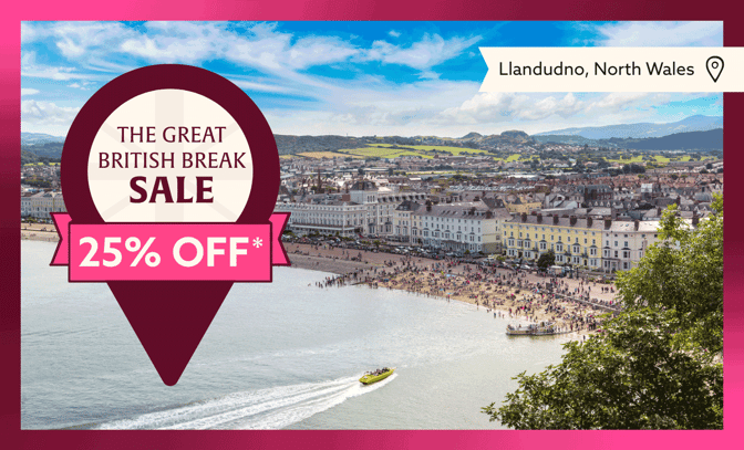 Llandudno, North Wales, featuring beachgoers, coastal buildings, and a sale banner highlighting 25% off for "The Great British Break."